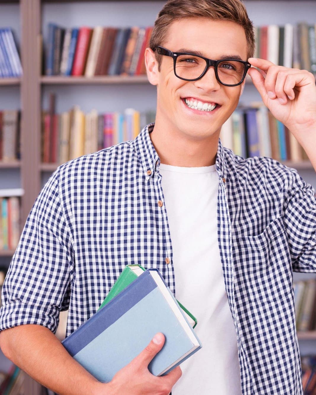 Học viên IELTS mỉm cười, ôm sách trước giá sách thư viện